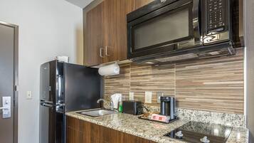 A modern kitchen with a stainless steel refrigerator, a microwave, a granite countertop, and a built-in oven.