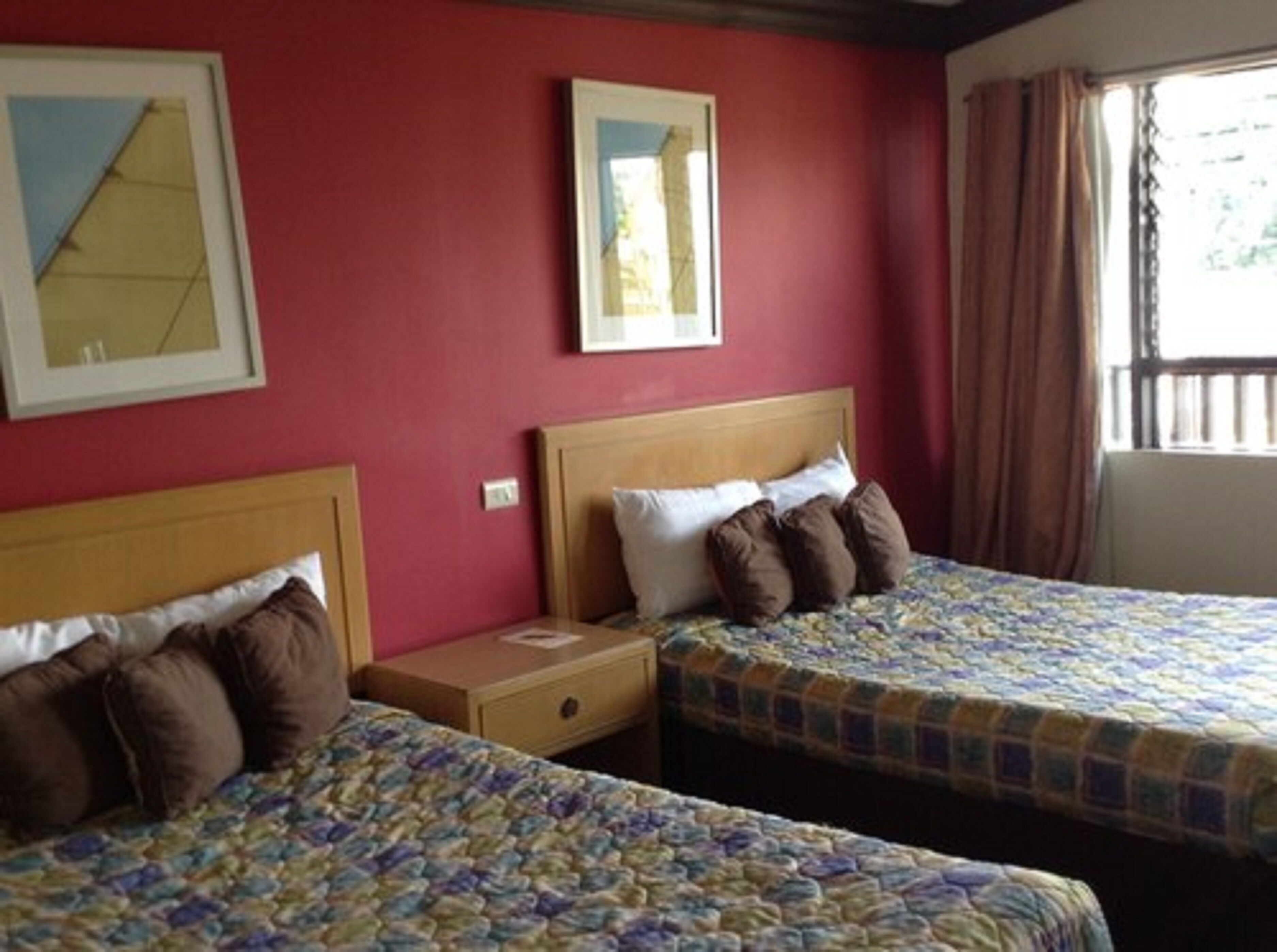 A hotel room with two beds, a wooden headboard, a nightstand, and a window with curtains.