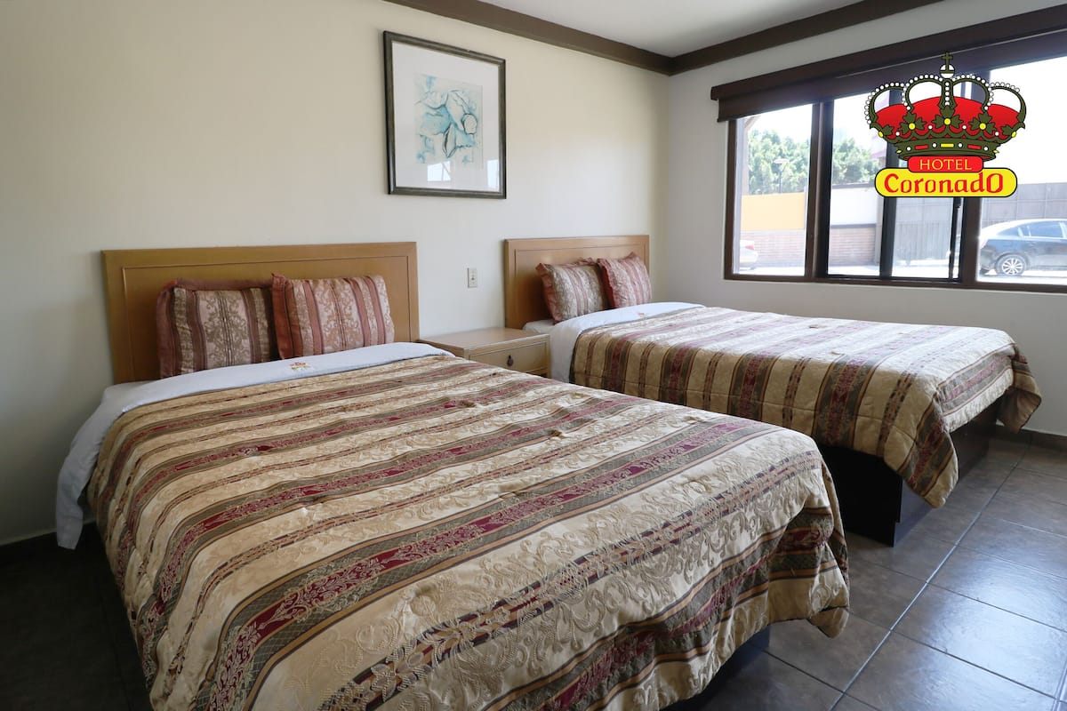 Une chambre d’hôtel avec deux lits, chacun recouvert d’une couvre-lit à motifs, une œuvre d’art encadrée au mur et une fenêtre donnant sur l’extérieur.