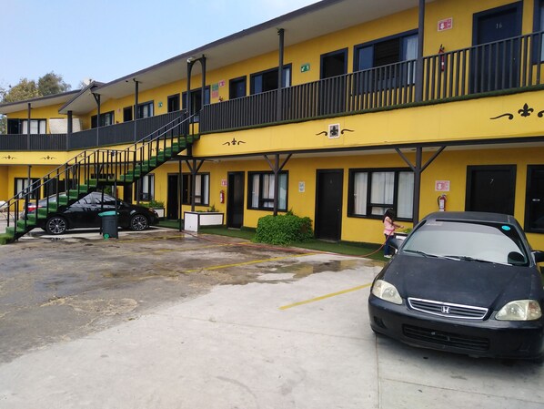 A yellow building with a balcony, a staircase, and a car parked in front. - Hotel Coronado (Ensenada)