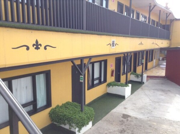 A yellow building with black window frames, a balcony, and white planters with green plants. - Hotel Coronado (Ensenada)