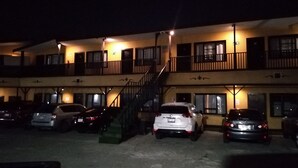 A multi-story building with a parking lot. There are several cars parked in front. The building has balconies and a staircase leading to the upper floors. - Hotel Coronado (Ensenada)