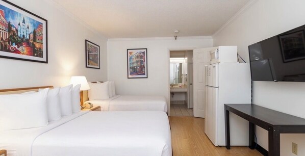 A hotel room with two beds, a desk, a television, and a refrigerator.