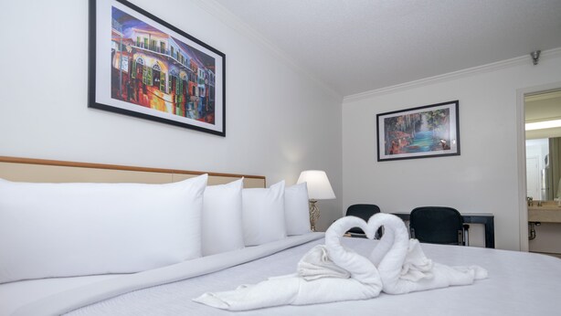 Una habitación de hotel con una cama grande, dos cuadros en las paredes, un escritorio con una silla y un espejo.