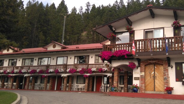 A two-story building with balconies adorned with flowers, a wooden door, and a sign indicating the establishment is open. - Gables Motel (Radium Hot Springs)