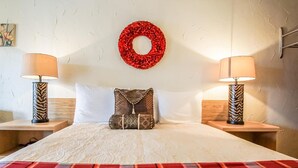 A neatly made bed with a plaid blanket, two bedside lamps with zebra-striped bases, a red wreath on the wall, and a pillow with a chain design. - Gables Motel (Radium Hot Springs)