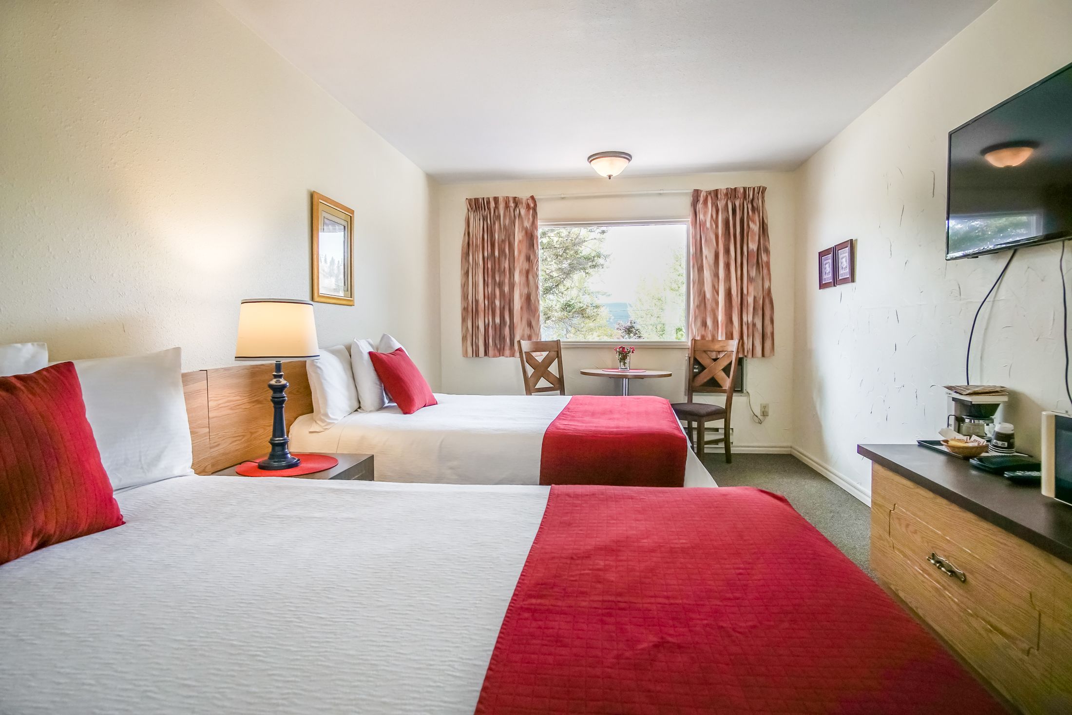 Une chambre d’hôtel avec deux lits, une télévision, un bureau, une chaise et une fenêtre avec des rideaux.