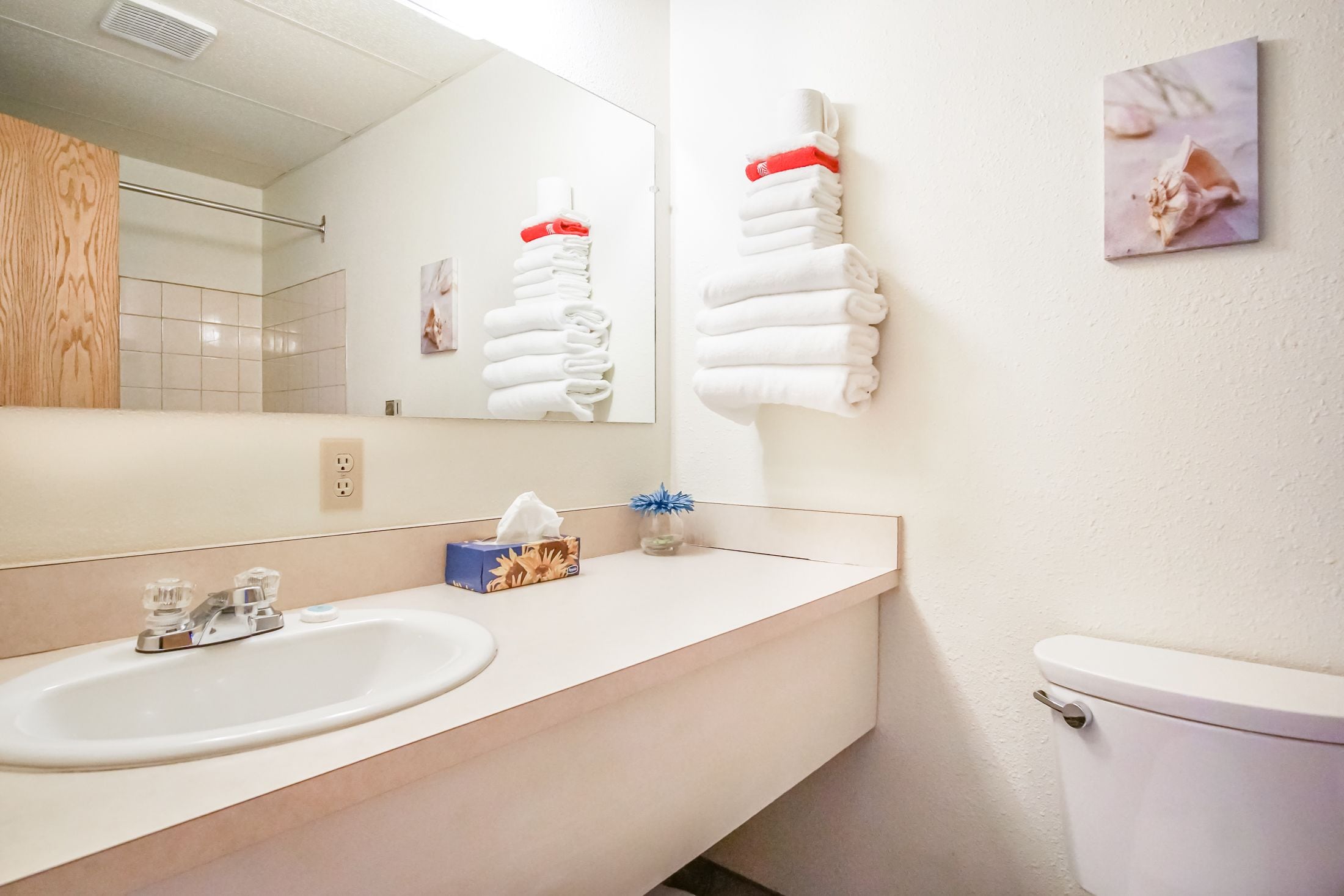 A modern bathroom with a sink, mirror, towel rack, toilet, and a framed picture on the wall.