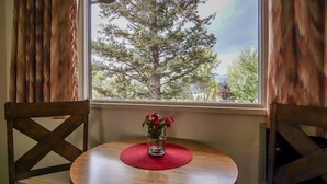 A round wooden table with a red placemat and a clear glass vase with red flowers. - Gables Motel (Radium Hot Springs)