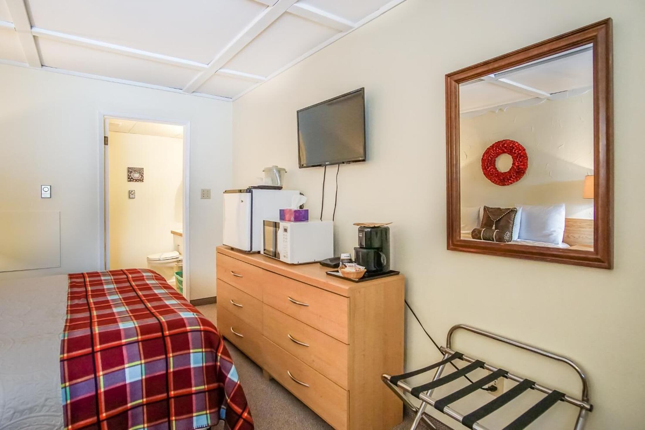 A bedroom with a bed, a dresser, a TV, and a mirror.