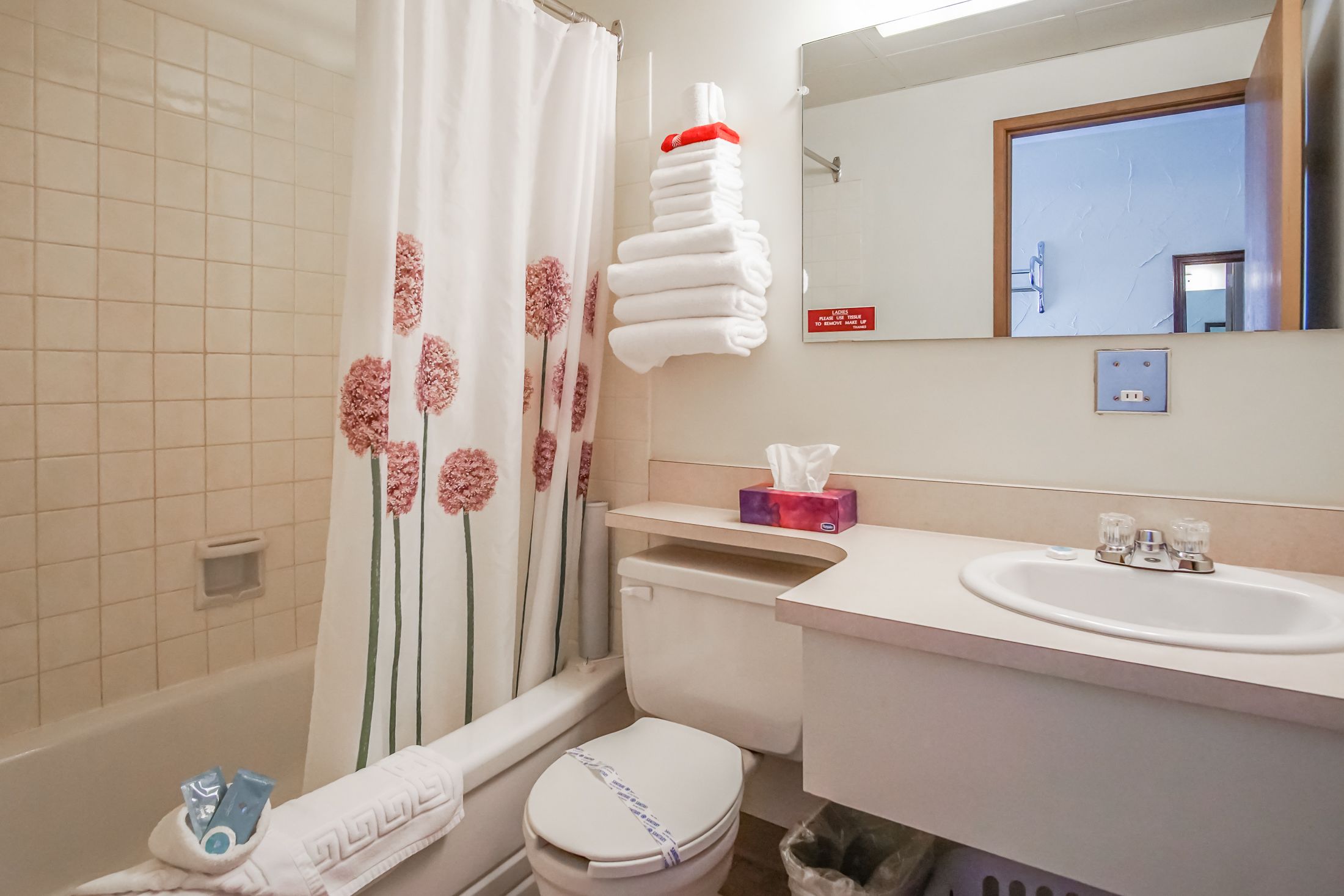 Et badeværelse med toilet, vask og bruseforhæng med blomstermønster.