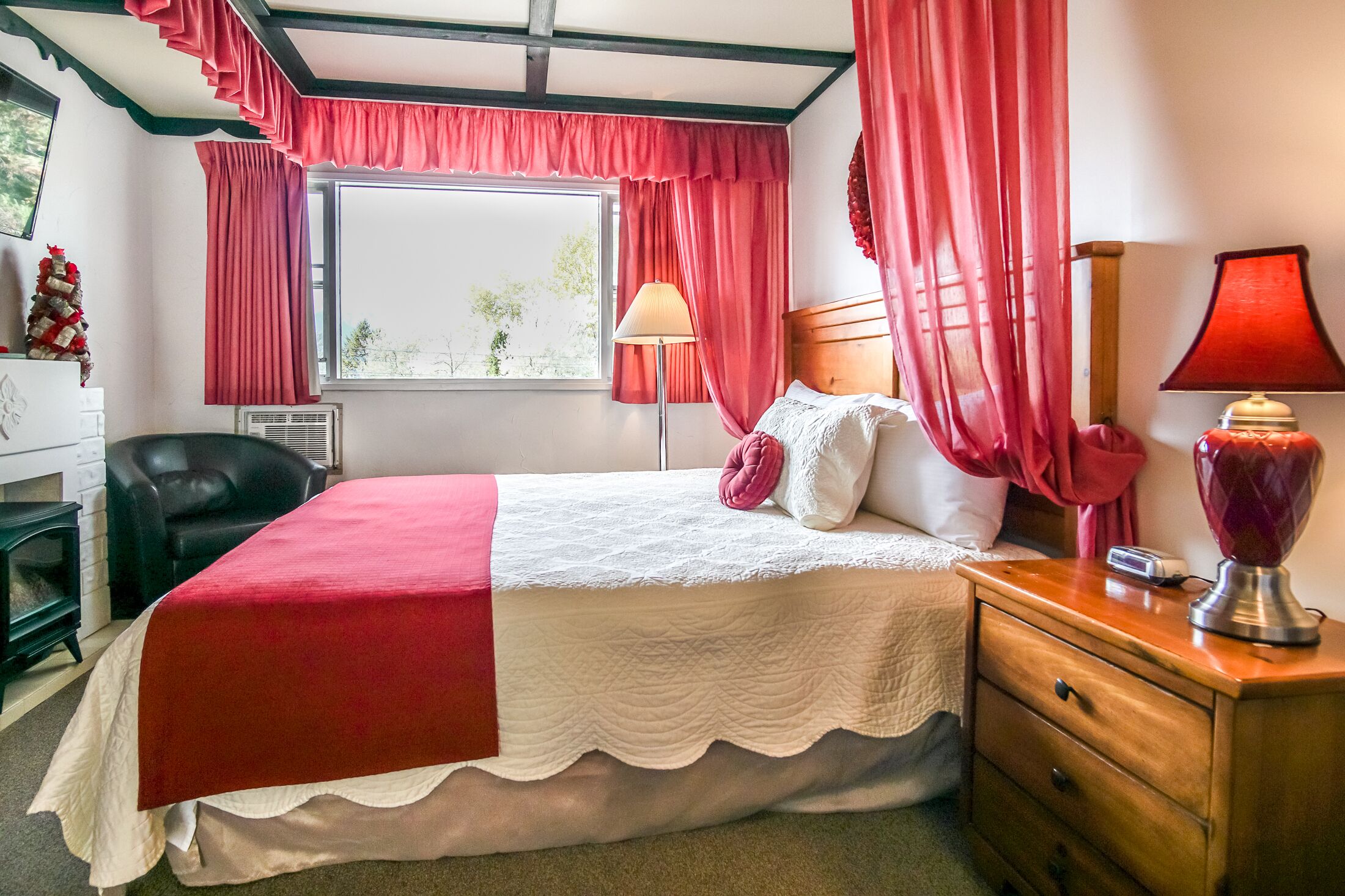Ein ordentlich eingerichtetes Schlafzimmer mit Bett, Nachttischlampen, einem Schminktisch und einem Fenster mit Vorhängen.