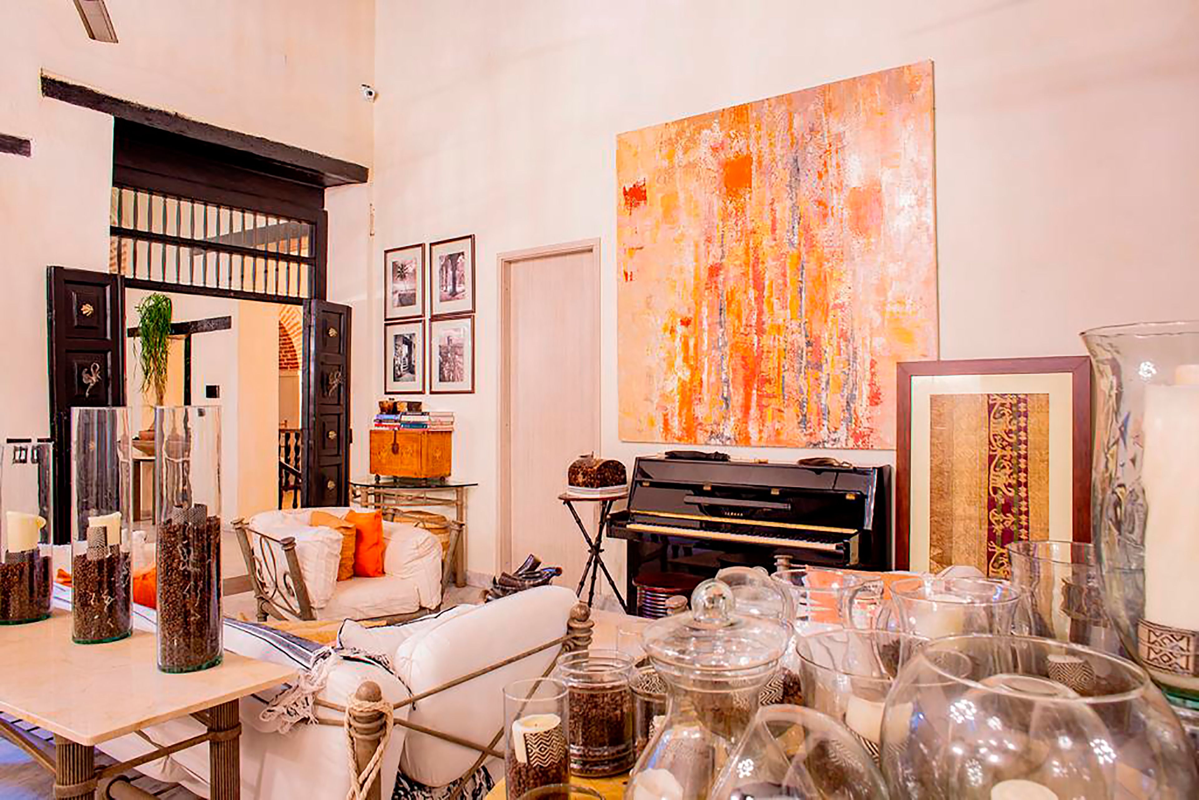 Een kamer met een piano, een groot abstract schilderij en diverse decoratieve objecten op planken en tafels.