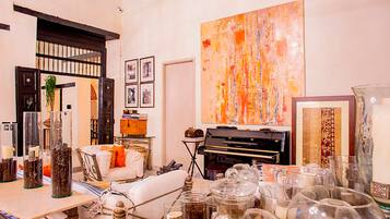 Een kamer met een piano, een groot abstract schilderij en diverse decoratieve objecten op planken en tafels.