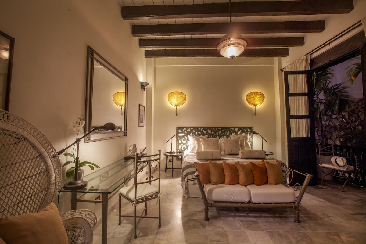 Una habitación bien iluminada con cama, sofá y mesa de comedor. Hay apliques de pared y una lámpara de techo.