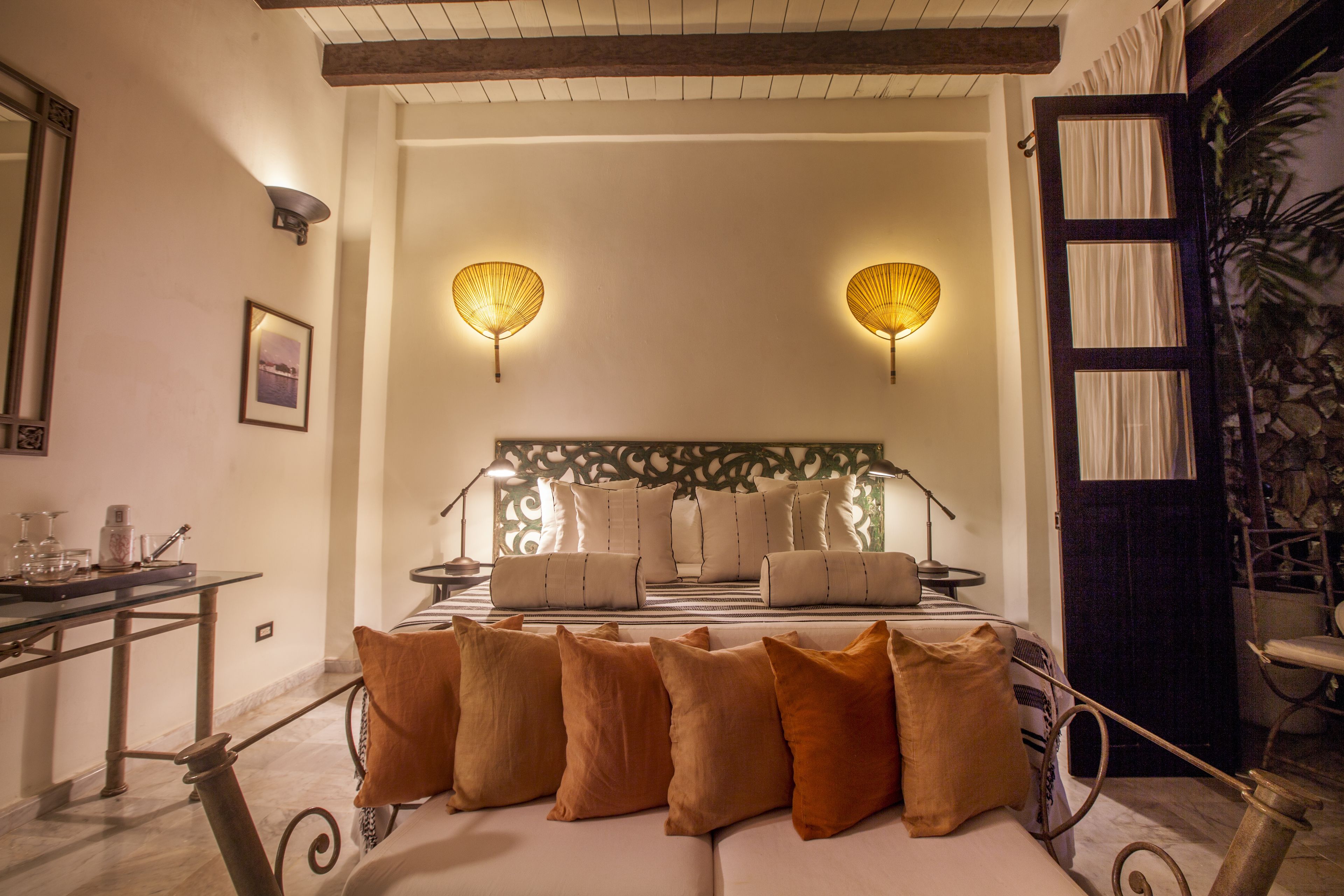 A bedroom with a bed, pillows, a nightstand, a lamp, and wall sconces.
