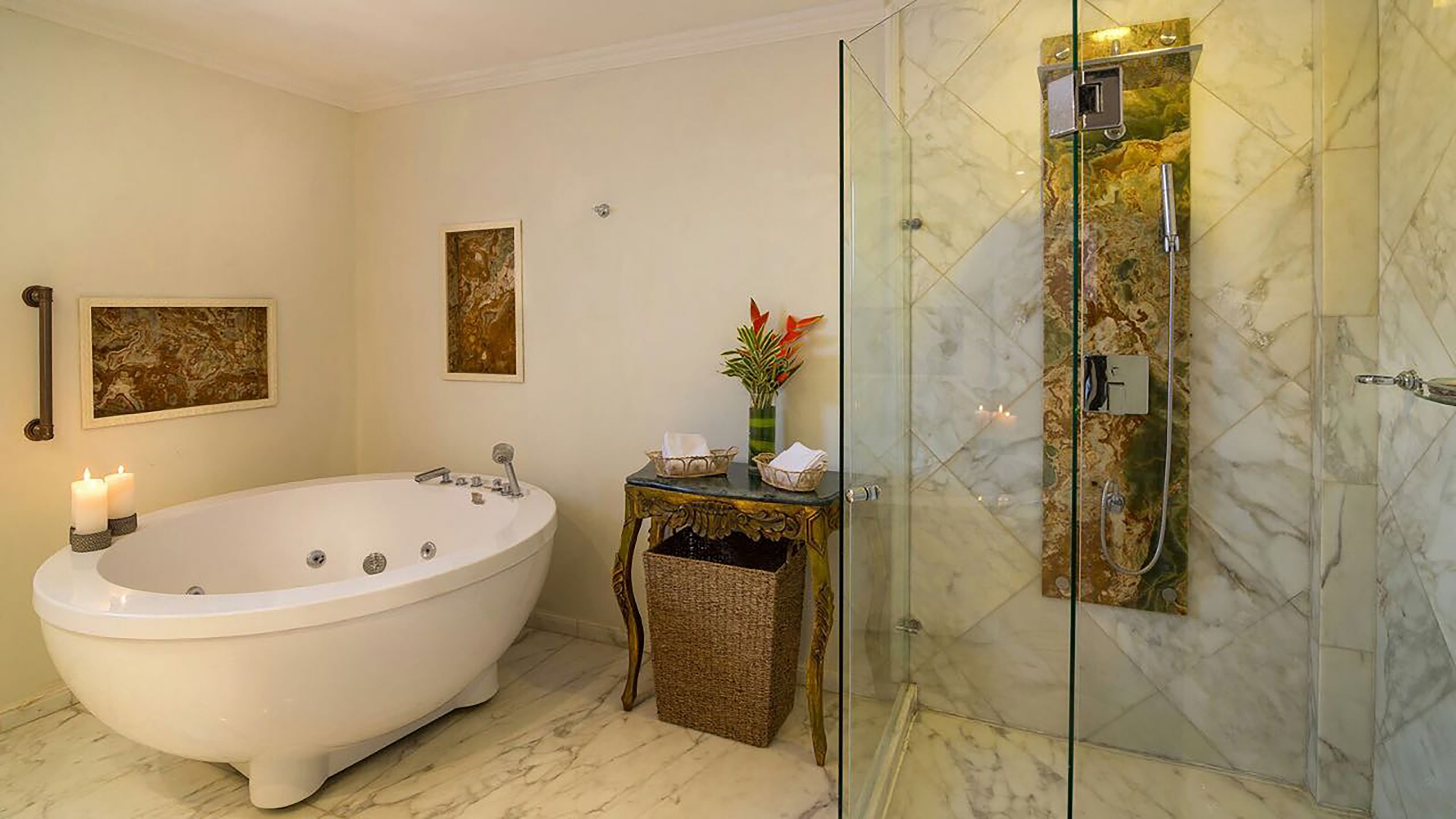 Un baño con una bañera independiente, ducha con cerramiento de vidrio, suelo de mármol y una obra de arte colgada en la pared.