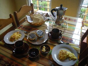 Une table mise pour le petit-déjeuner, avec des assiettes d’œufs brouillés, des toasts et une cafetière, entourée de chaises.
