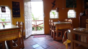 Un espace repas comprenant une table et des chaises, une porte donnant sur l’extérieur et une fenêtre offrant une vue sur la verdure.