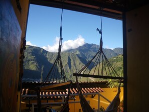 Uma cadeira de rede suspensa no teto, um telhado de azulejos e vista para montanhas.