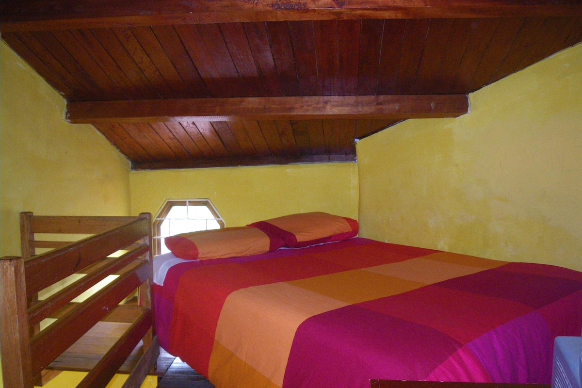 A small, single-bed room with a wooden ceiling and yellow walls.