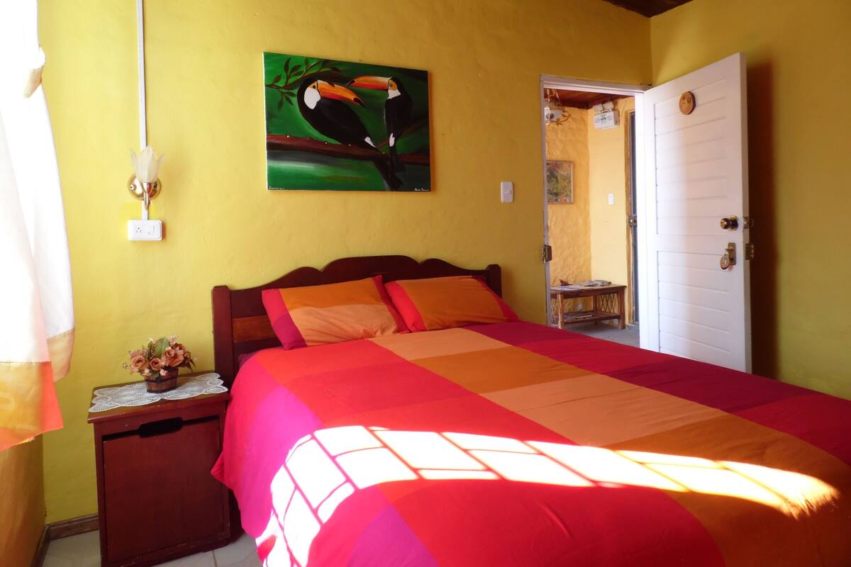 A room with a bed, a nightstand, a painting, a door, and a window.