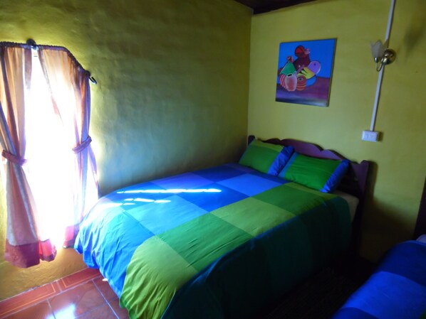 Una habitación con cama, cortinas, un cuadro en la pared y un interruptor de luz.