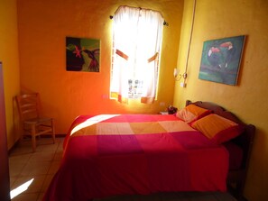 Une pièce comprenant un lit, une chaise, une fenêtre avec des rideaux et deux tableaux accrochés au mur.