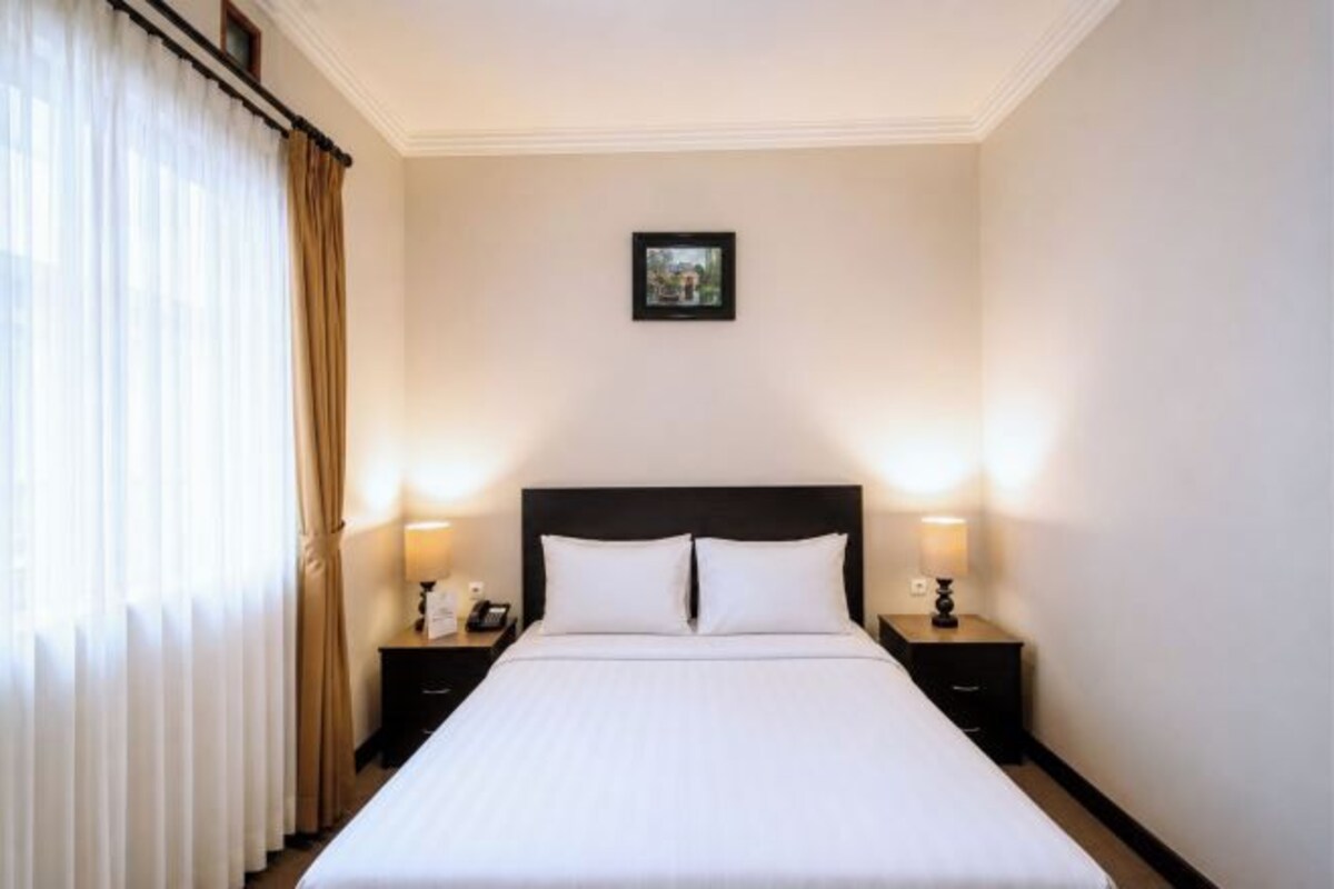 A hotel room with a large bed, two bedside tables with lamps, a framed picture on the wall, and a window with curtains.