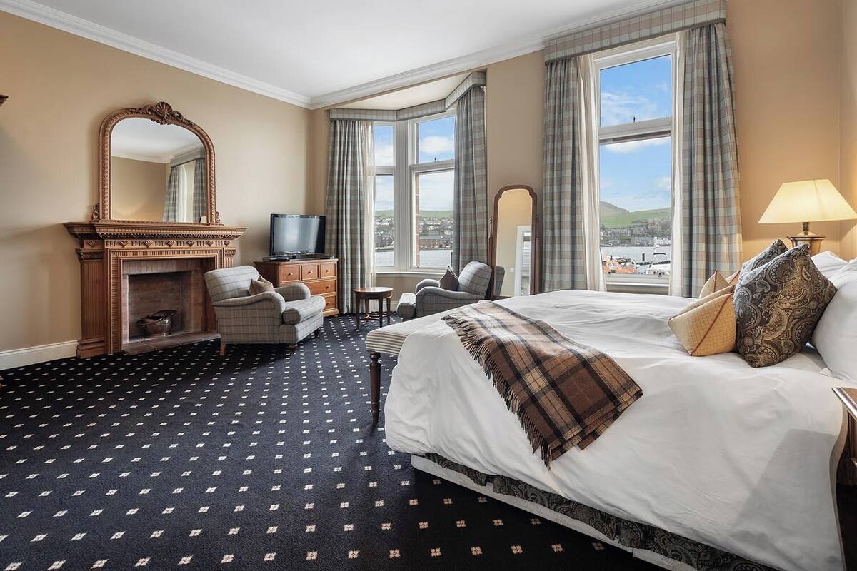 A hotel room with a large bed, a fireplace, a television, and a view of the outside.