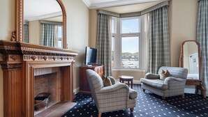 A room with a fireplace, two armchairs, a television, and a large window with curtains.