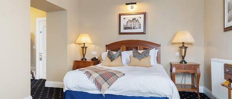 A hotel room with a large bed, two bedside tables with lamps, a framed picture on the wall, and a radiator.