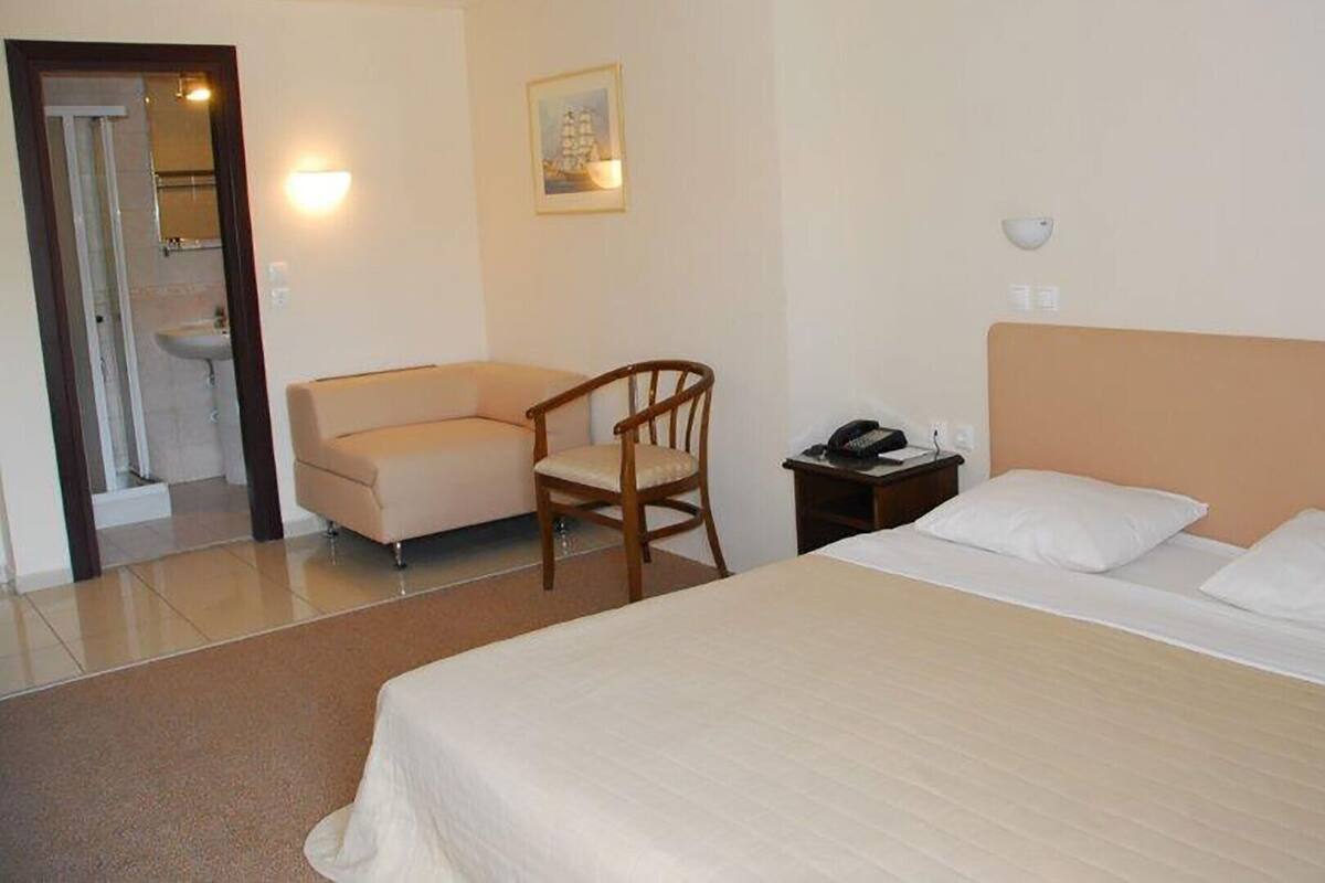 Une chambre d’hôtel comprenant un lit, une chaise, un bureau avec un téléphone et une lampe fixée au mur.