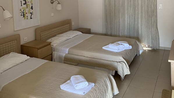 Quarto de hotel com duas camas, uma mesa de cabeceira, um relógio na parede e uma cortina.