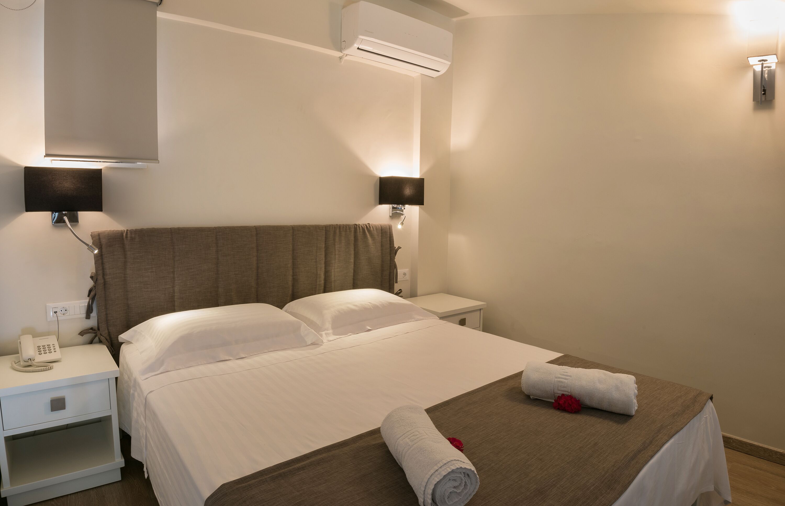 Habitación de hotel con una cama, dos mesitas de noche, un teléfono y un aire acondicionado instalado en la pared.