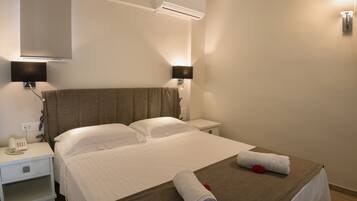 Habitación de hotel con una cama, dos mesitas de noche, un teléfono y un aire acondicionado instalado en la pared.