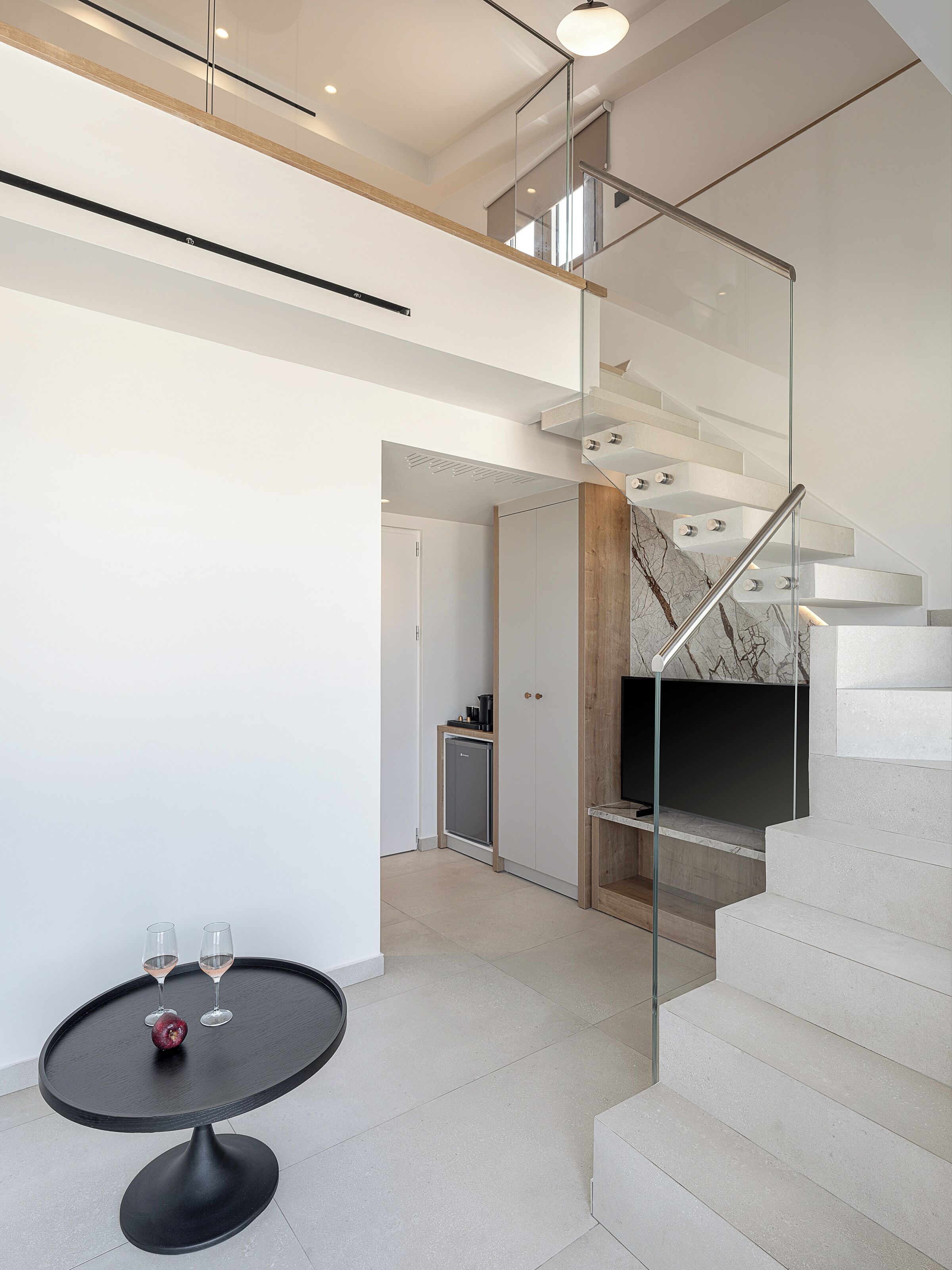 Un interior moderno con una escalera, una mesa de comedor con vasos y una pequeña zona de cocina.
