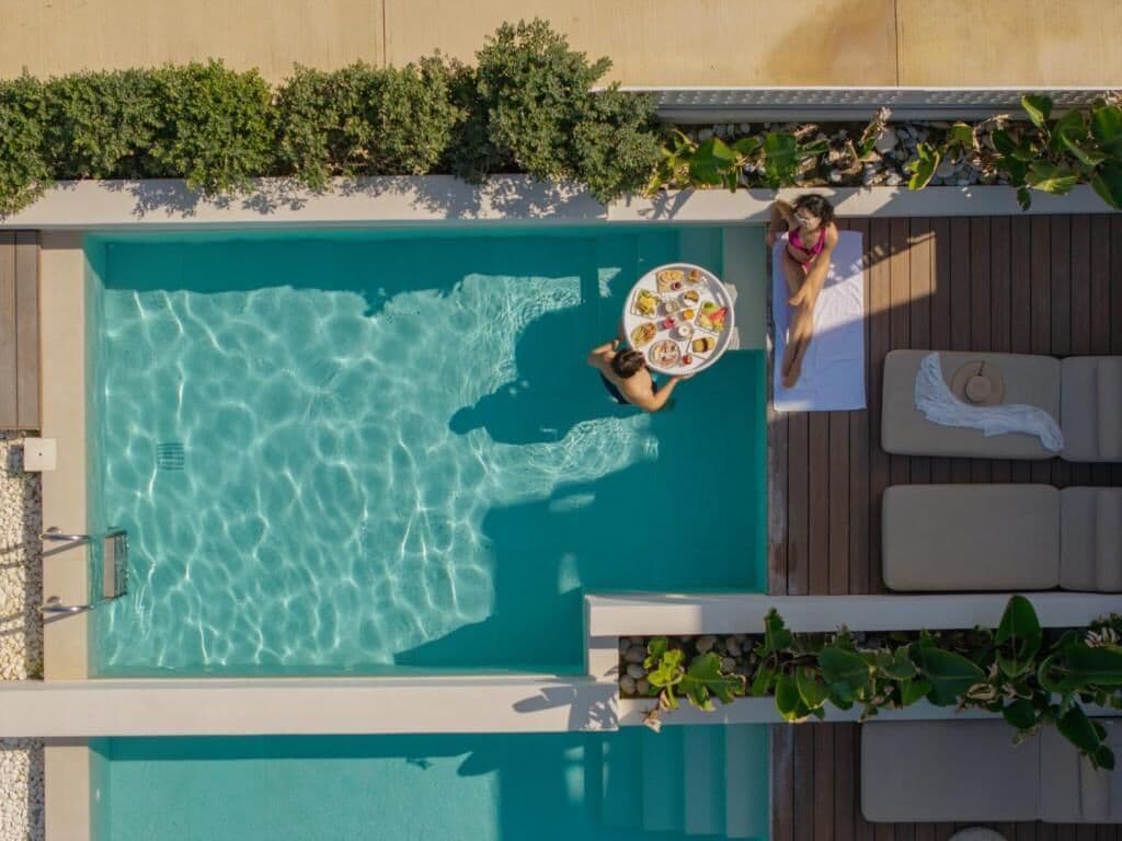 An aerial view of a swimming pool with a deck area, lounge chairs, and a dining table.