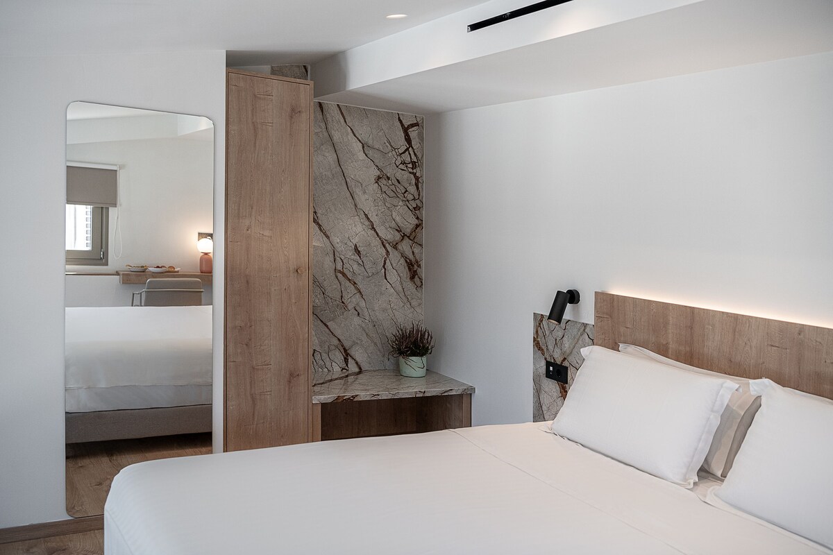 A modern bedroom with a large bed, a marble accent wall, a wooden headboard, and a small bedside table with a plant.