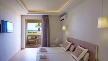 A hotel room with two beds, a TV, a balcony with a view of the beach, and a chair.