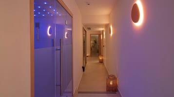 A hallway with a glass door on the left, a wooden door at the end, and a wall-mounted light fixture on the right.