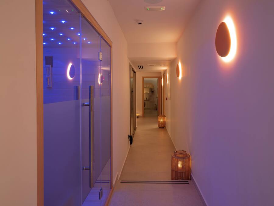 A hallway with a glass door on the left, a wooden door at the end, and a wall-mounted light fixture on the right.