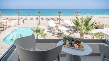Een balkon met uitzicht op een strand, een zwembad en een fruitschaal.