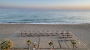 A beach with rows of sun loungers and umbrellas, palm trees, and the ocean. - Iperion Beach (Rethymno)