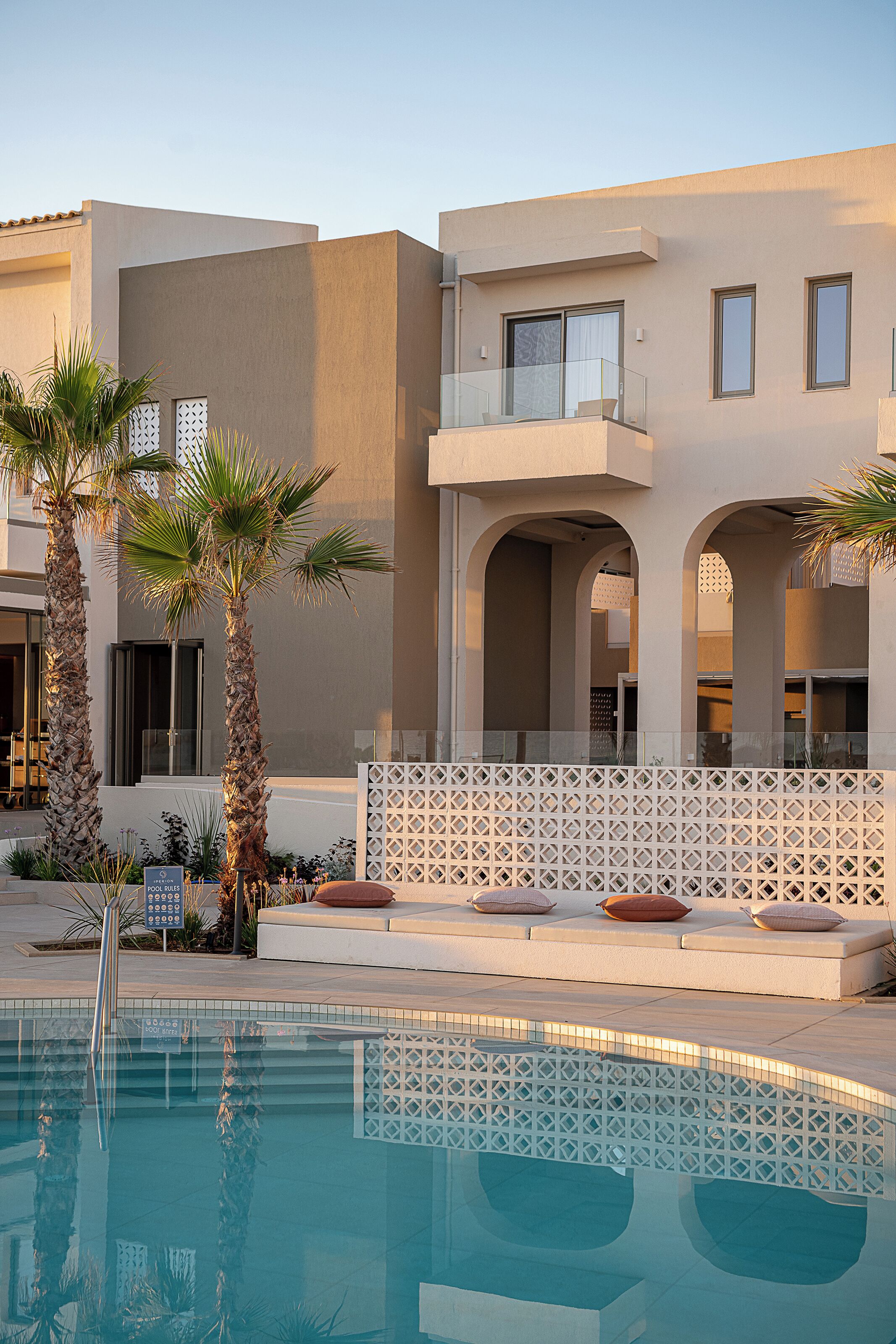 A pool area with a clear view of the pool, a palm tree, and a building with a balcony.