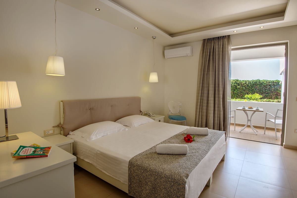 A hotel room with a bed, bedside table, lamp, and a view of the balcony.