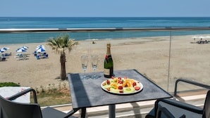 A table with a fruit platter, two glasses, and a bottle of champagne on a balcony overlooking a beach with umbrellas and lounge chairs. - Iperion Beach (Rethymno)