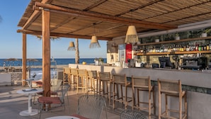 A beachside bar with wicker chairs and tables, a bar counter with a variety of bottles, and a view of the sea. - Iperion Beach (Rethymno)