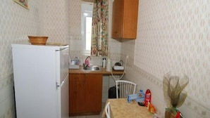 A small kitchen with a refrigerator, a sink, and a dining table with chairs. - Sevi Sun Studios and Apartments (Kos)