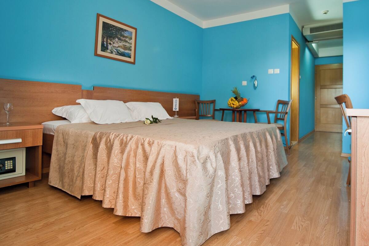 Habitación de hotel con cama, mesita de noche, escritorio, silla y pequeña mesa con fruta.